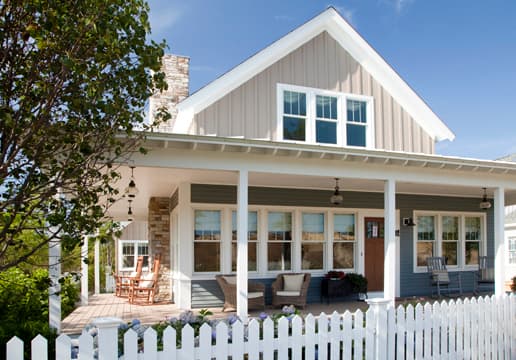 house-fence-ideas House with beige board and batten siding behind a white picket fence.